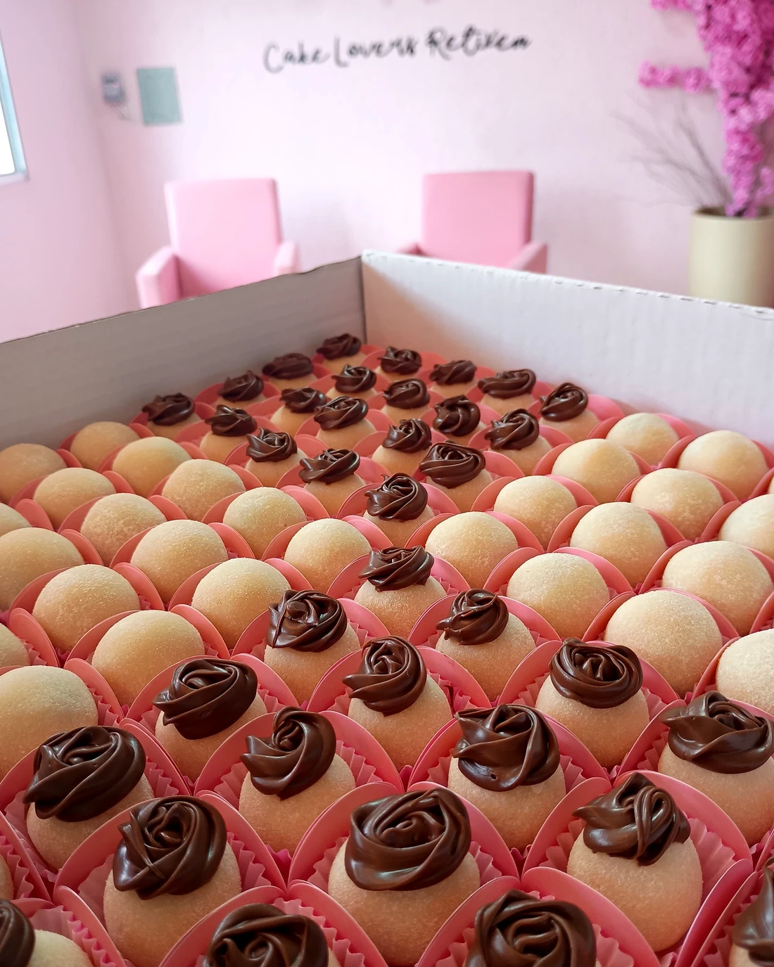 Caixa de docinhos em forminhas rosa, metade com rosinhas de chocolate confeitadas por cima
